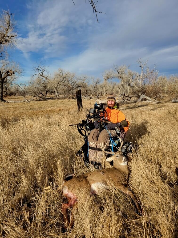Hunter in a tracked chair sitting in a Colorado field with a harvested deer.