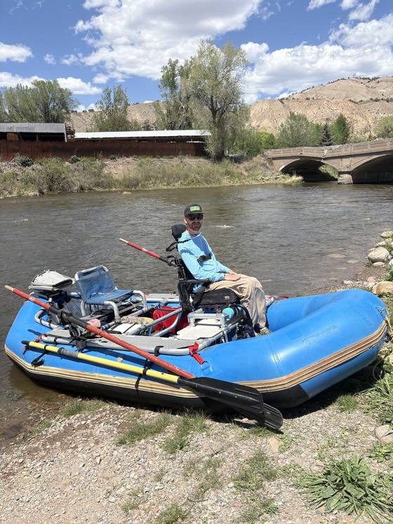Participant seated in an adaptive frame on a blue raft at the edge of a Colorado river.