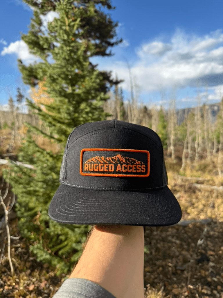 Hand holding up the black 7-panel in front of a pine tree, orange patch facing the camera.