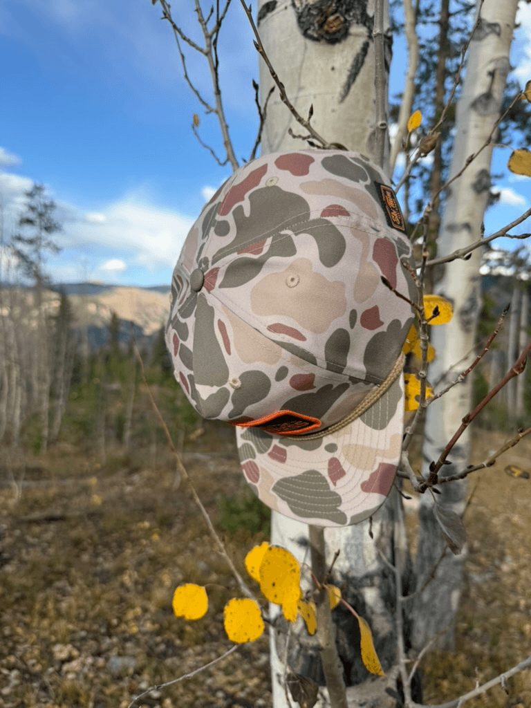 Camo rope hat hanging on an aspen branch among yellow fall leaves.